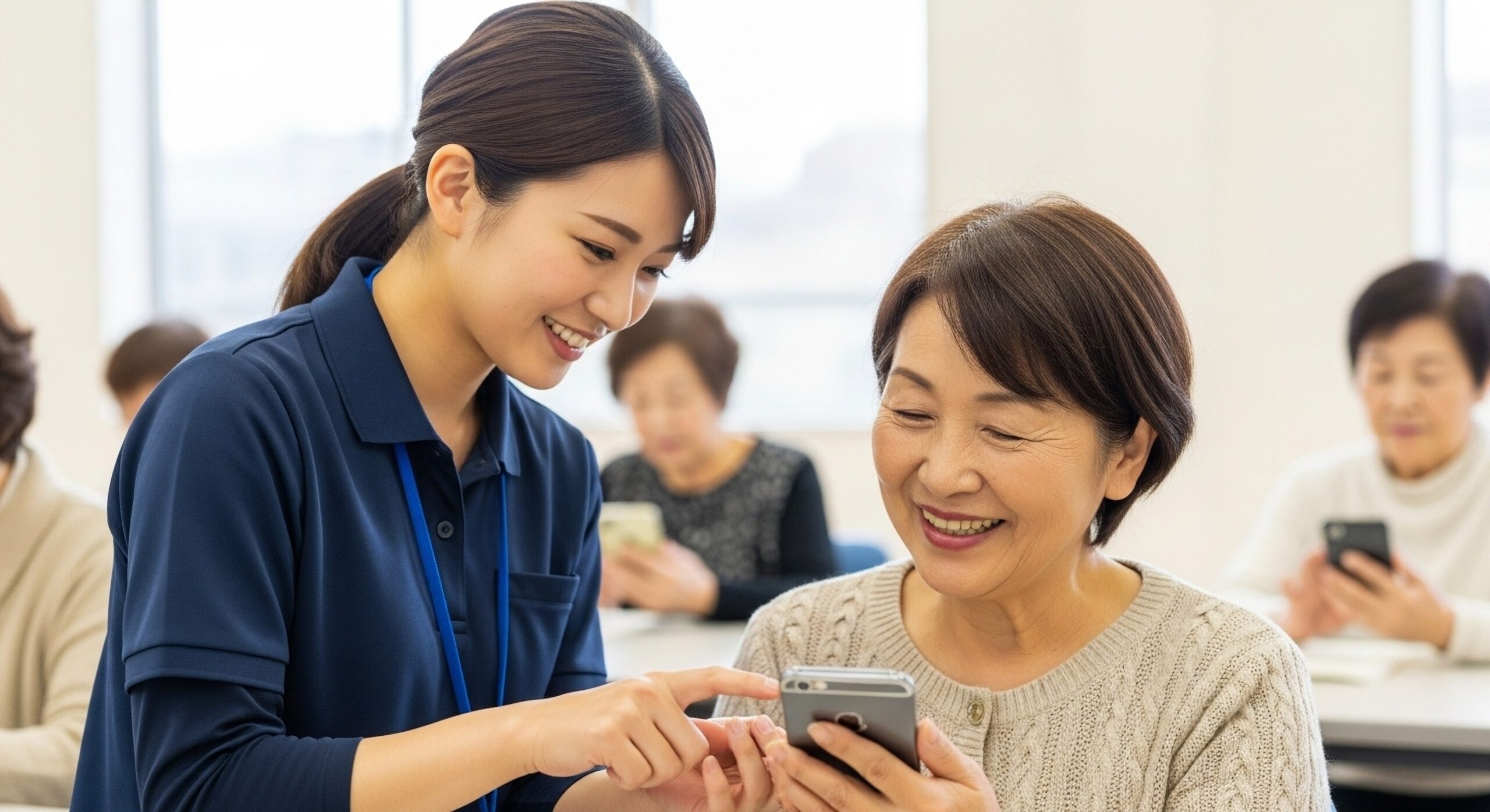 神戸市のスマホ相談窓口で、学生が高齢者にスマートフォンの操作方法をマンツーマンで説明している様子